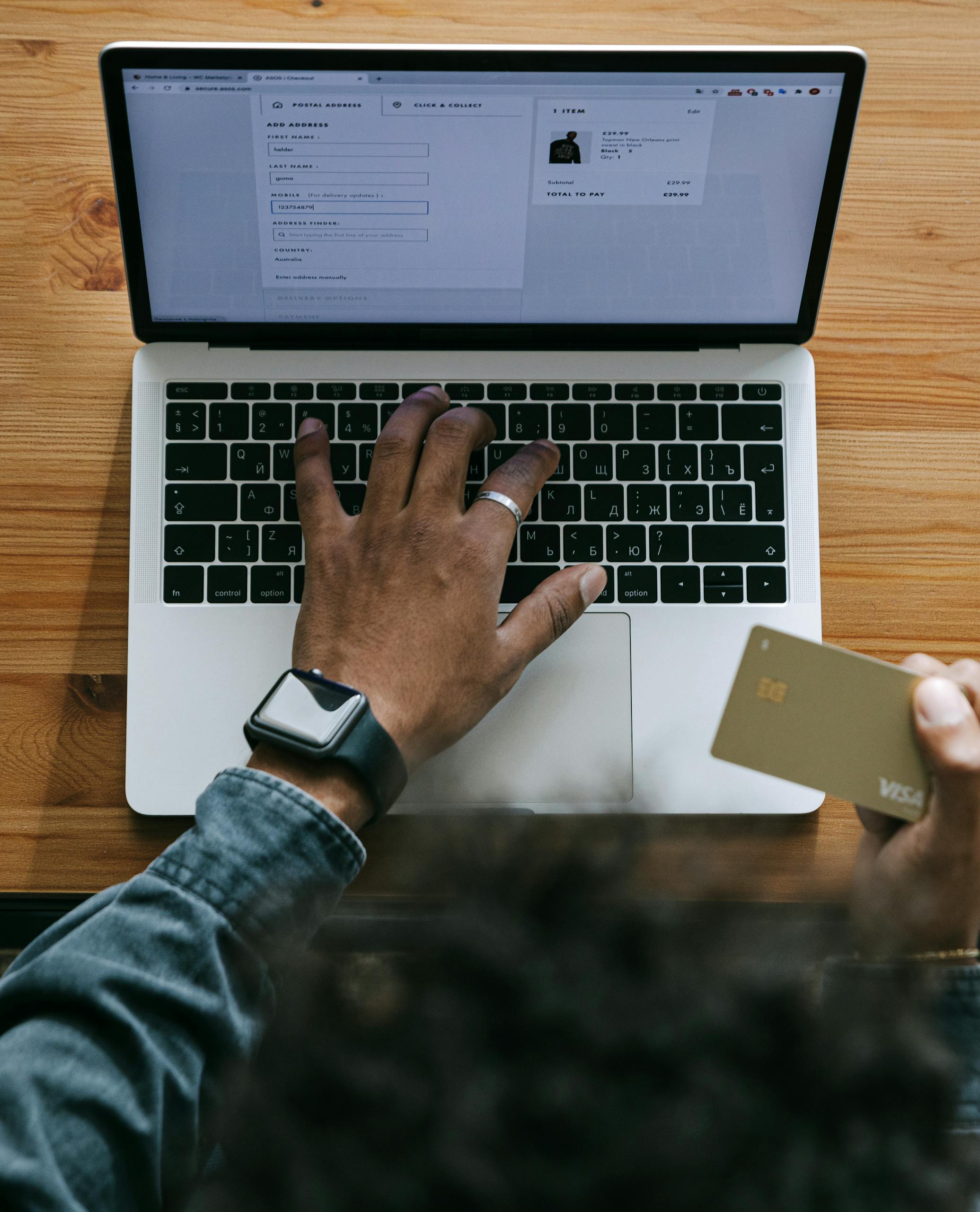 Person using a laptop to make an online purchase with a credit card on a wooden table.